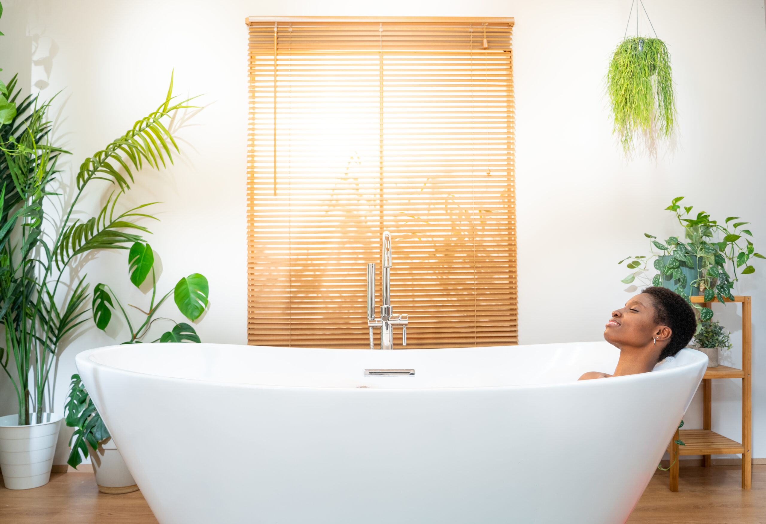 Smiling African attractive woman wearing headphones relaxing and dancing in foam bath in bathroom.